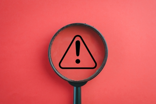 View through a magnifying glass on Exclamation mark or Warning sign over red background